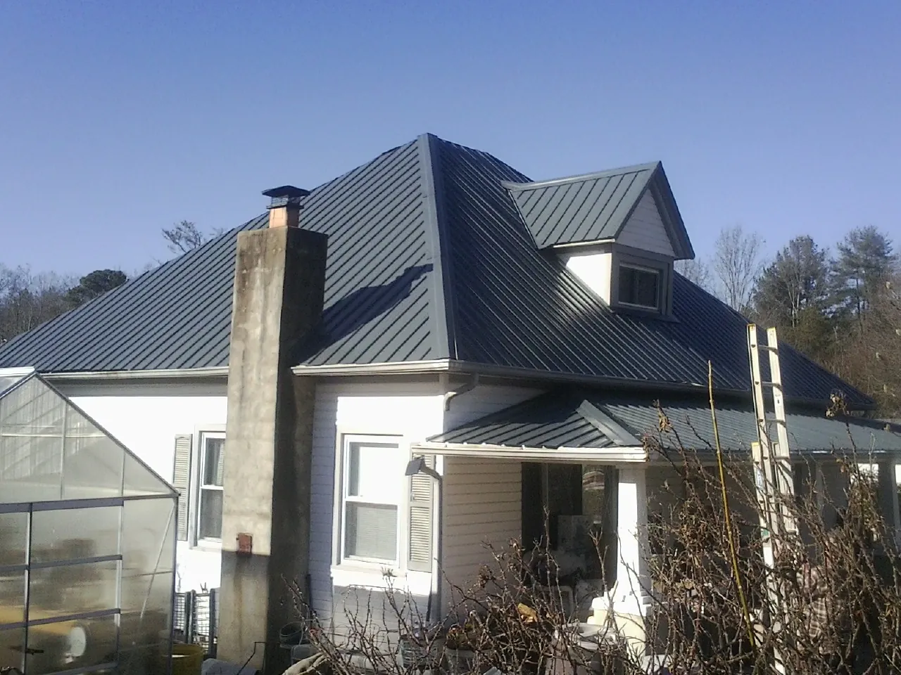 Dark blue standing seam metal roof on a white farmhouse with dormer — Slate & Tile Roof Repair by Roofing Brothers in Highland Lake