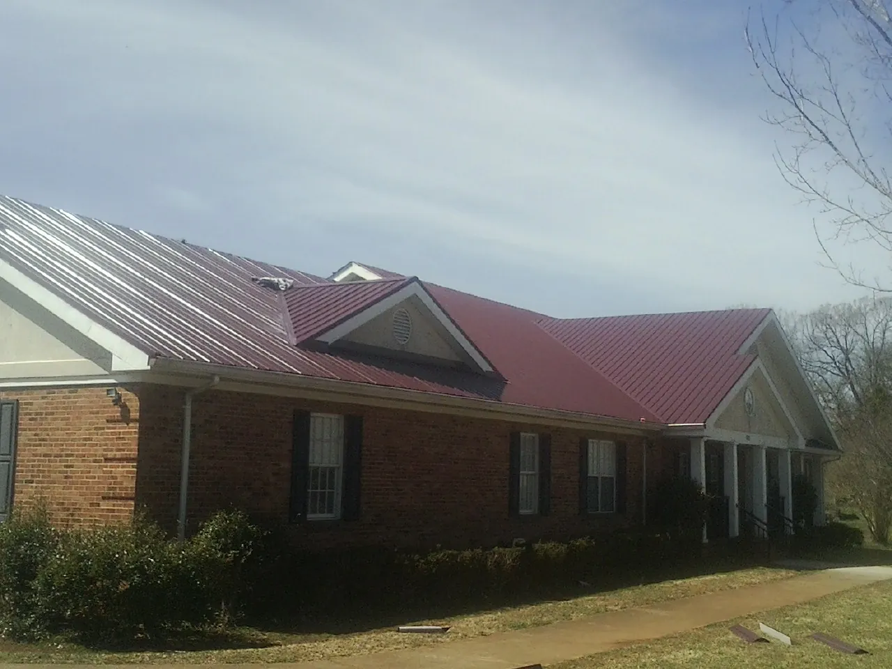 Red metal roof with gabled entries on a long brick building, from a Hail Damage Roof Repair job in Highland Lake