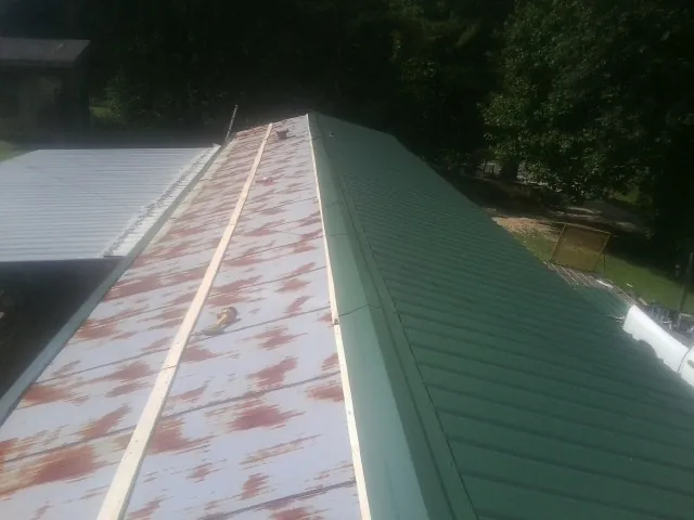 Old rusted panels beside newly installed green metal roofing — Wind Damage Roof Repair by Roofing Brothers in Highland Lake