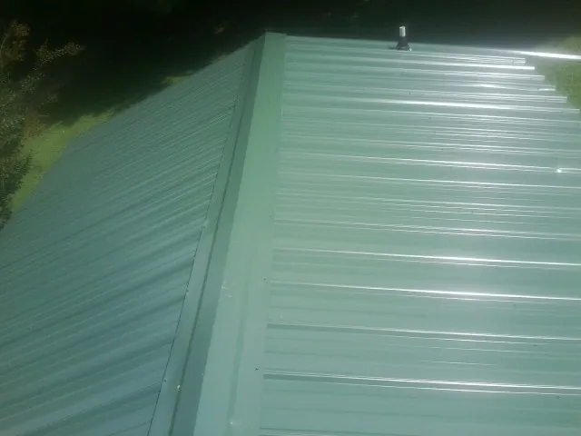 New green metal panels meeting at the ridge of a roof — Flat Roof Repair work by our crew in Highland Lake