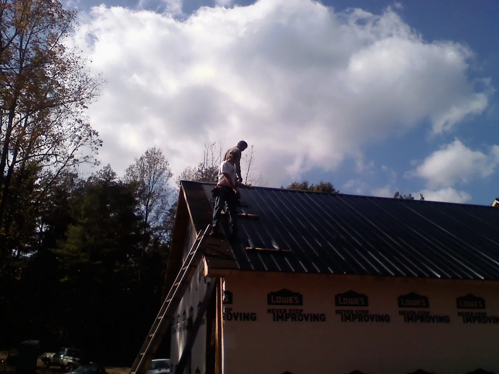 Roofer fastening dark metal panels high against a cloudy sky, from a Roof Inspection job in Highland Lake