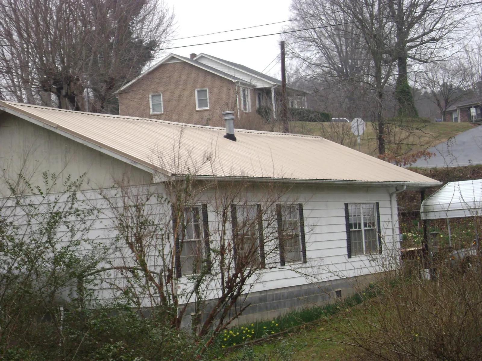 Tan metal roof on a white sided house set into a hillside — Commercial Roofing by Roofing Brothers in Highland Lake