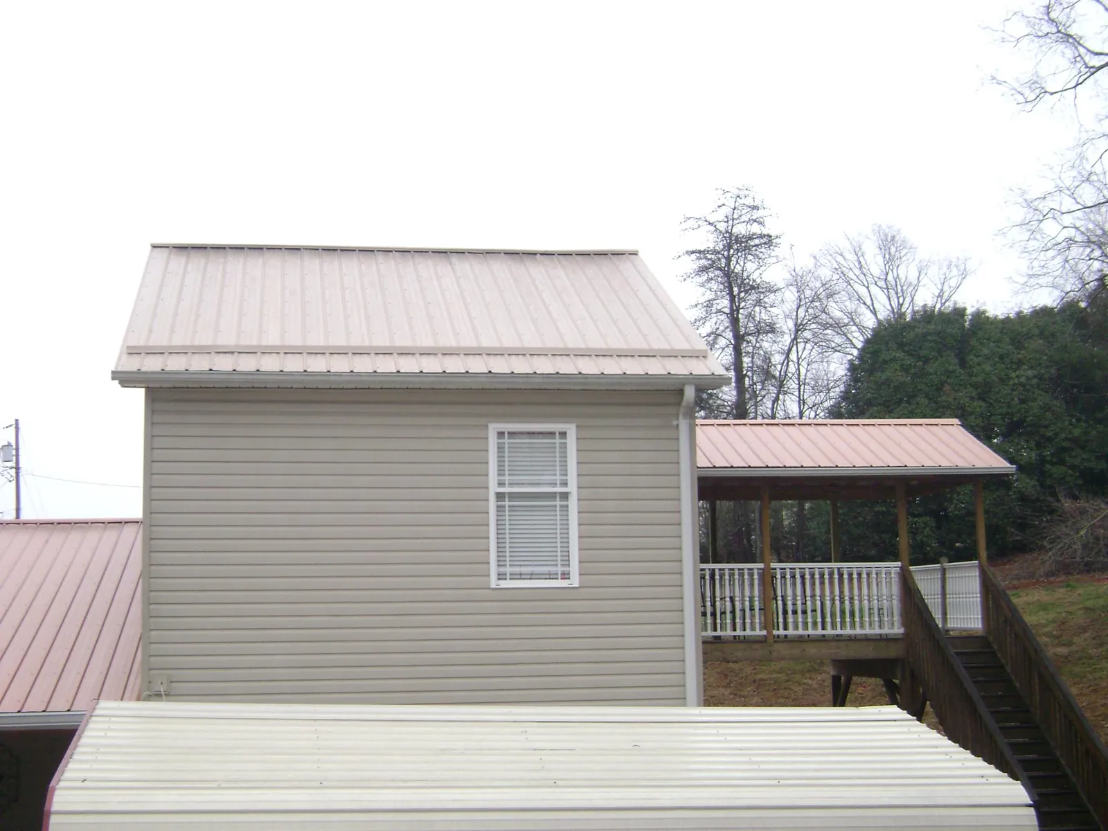 Tan metal roofs on a two story addition and attached porch, from a Roof Replacement job in Highland Lake